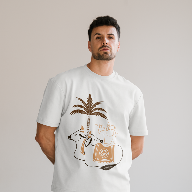 A man wearing a white crewneck t-shirt with a graphic print of a A2 cow, a palm tree, and a rider playing a flute, set against a solid light gray background.