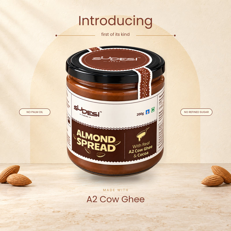 A jar of Sudesi Almond Spread with A2 Cow ghee and cocoa, presented on a light beige textured background with decorative almonds and promotional text saying " Introducing the first of its kind, made with A2 cow ghee"